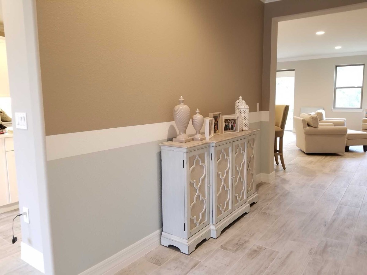 A hallway painted greige above and sage below, divided by a crisp white horizontal band that continues around the corner