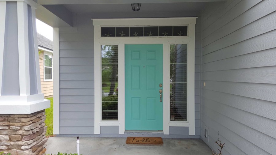 A teal painted front door set in grey lap siding with white trim and a stone base