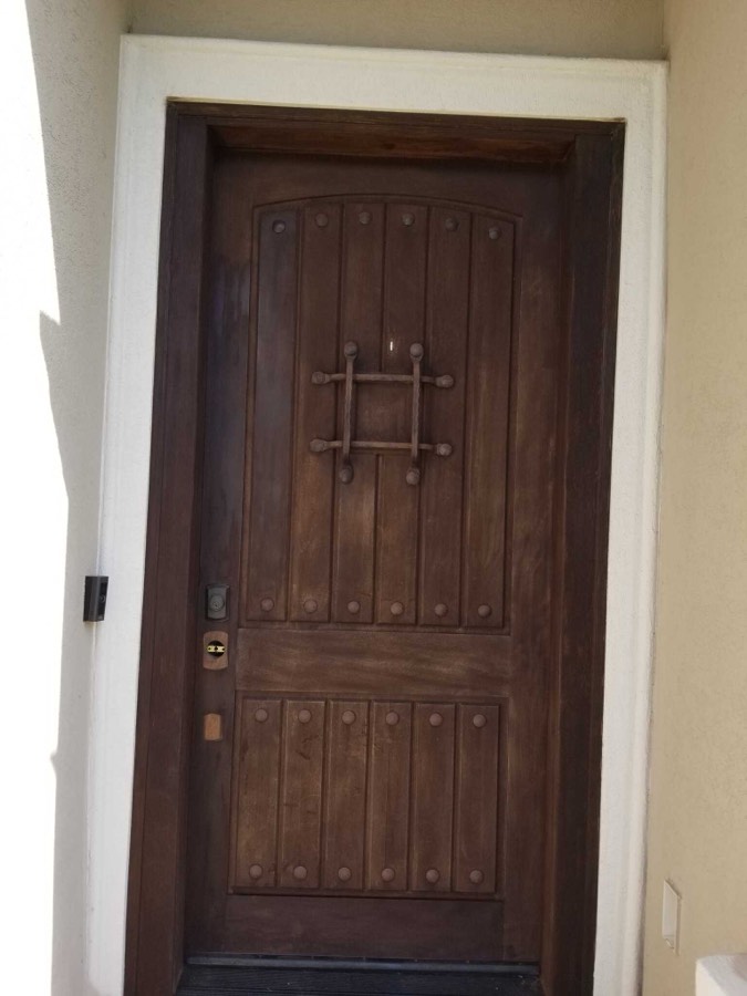 A rustic stained wood front door with a speakeasy grille and iron studs