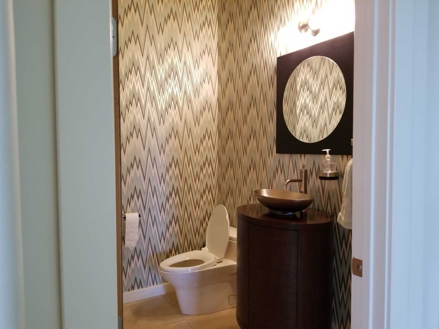 A powder room with a patterned chevron wallpaper accent wall, vessel sink and dark framed mirror