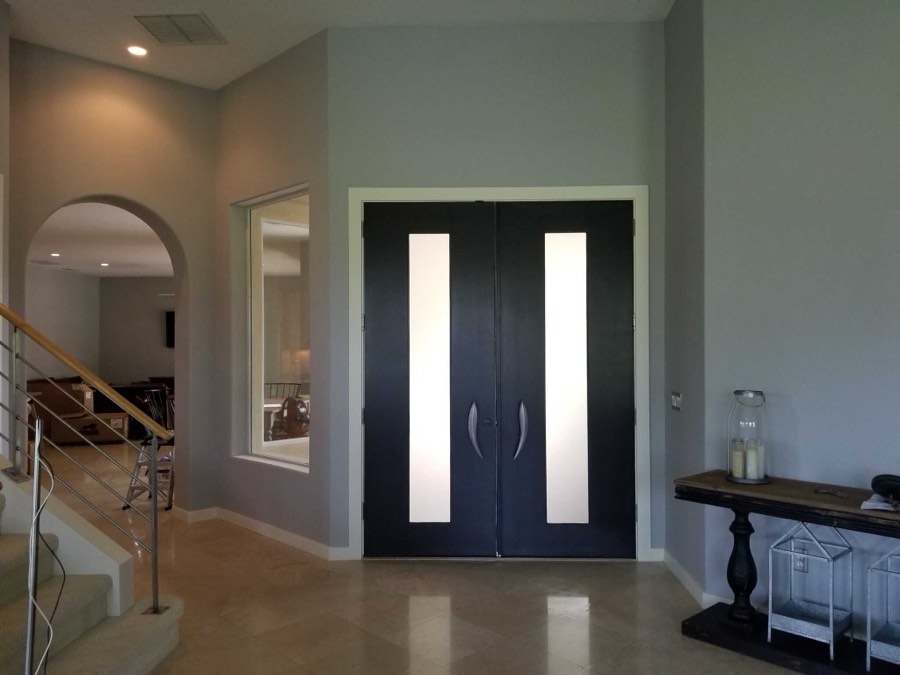 An entry hall with dark double doors, sage walls and a staircase beyond