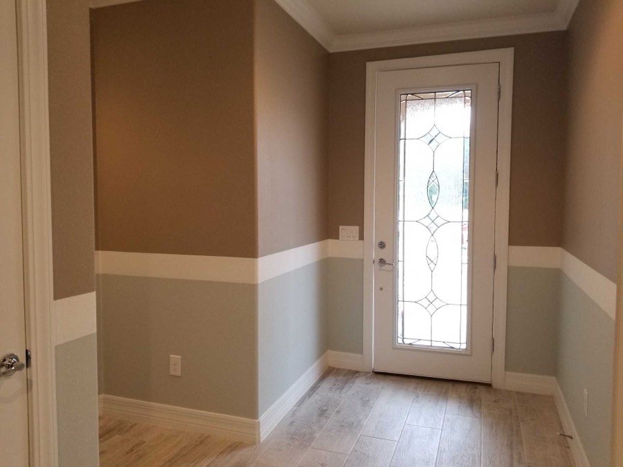 A foyer painted in two tones with a white band, beside a leaded glass front door