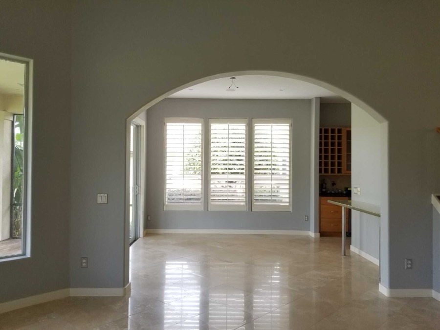 An open interior with arched openings, plantation shutters and travertine floors painted in soft sage grey